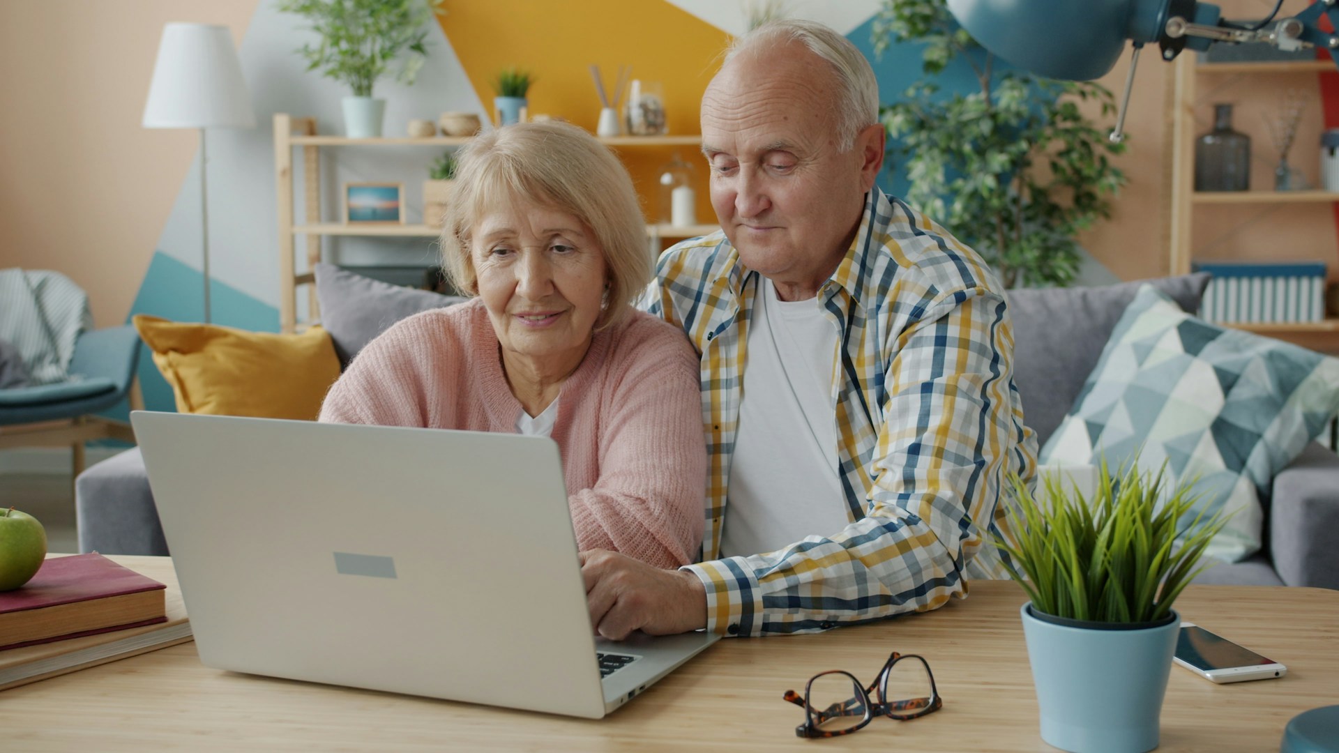 Älteres Paar schaut gemeinsam lächelnd auf einen Laptop