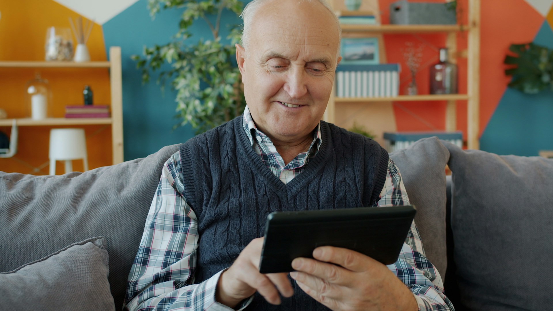 Älterer Mann sitzt entspannt auf dem Sofa und bedient lächelnd ein Tablet